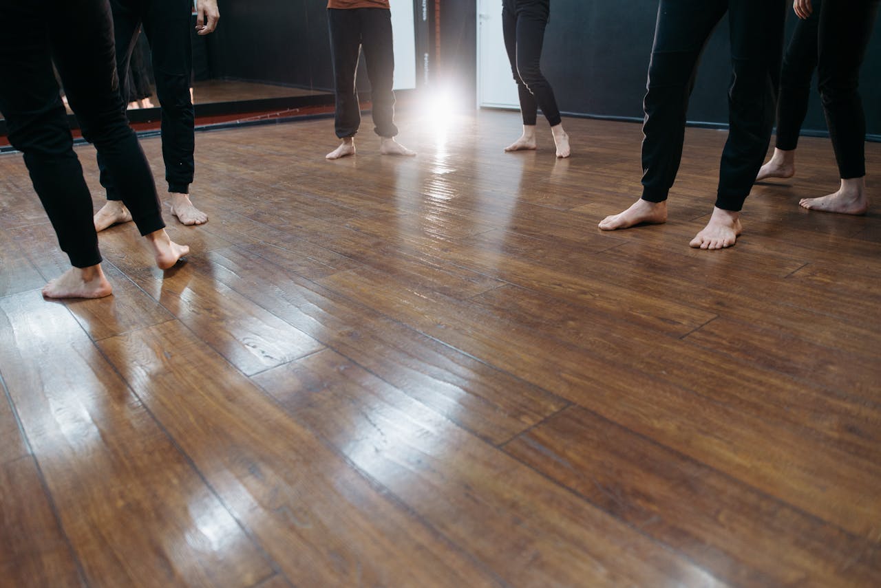 A group of people standing barefoot on a polished wooden floor indoors.